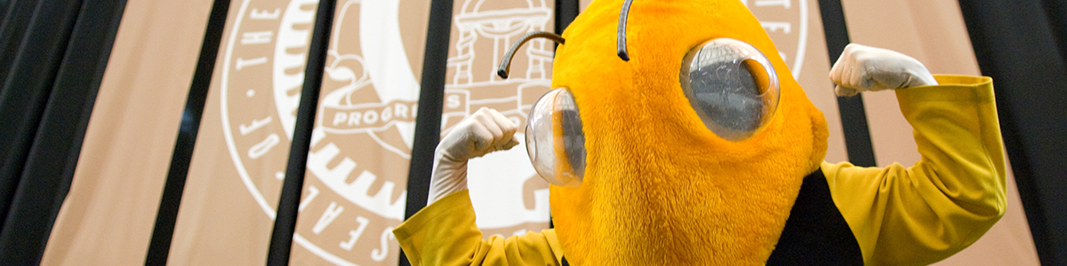 Georgia Tech’s mascot, Buzz, stands in front of the Georgia Tech seal, which reads ’progress and service,’ at an undergraduate student graduation ceremony