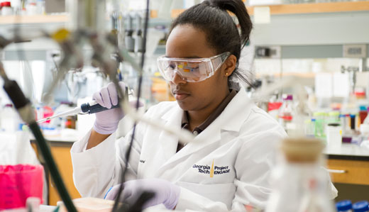 A student in a research laboratory at Georgia Tech holds a pipette while wearing protective eyewear, gloves, and a lab coat.