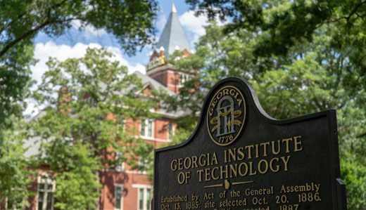 A sign detailing the history of the establishment of Georgia Tech is in the foreground, with campus greenery and Tech Tower in the background.