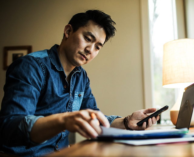 A person is looking at something in a notebook while holding a cell phone in their left hand.