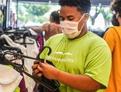 homem de máscara, vestindo verde, dentro do bazar da gerando falcões olhando uma peça de roupa