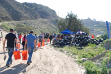 A group of volunteers walk down to a clean up site holding buckets and shovels.