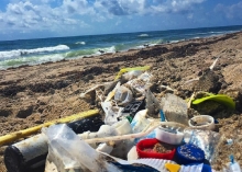 Plastics and a glass bottle lay on the sand.