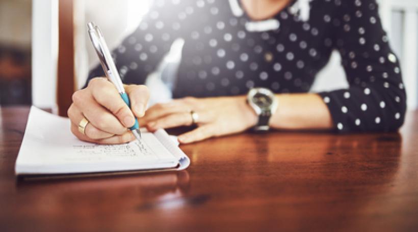 Person at desk writing list in notebook