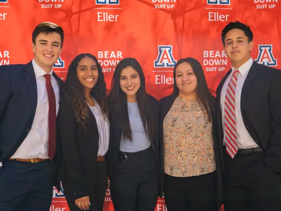 Graduate students smiling in front of Eller banner