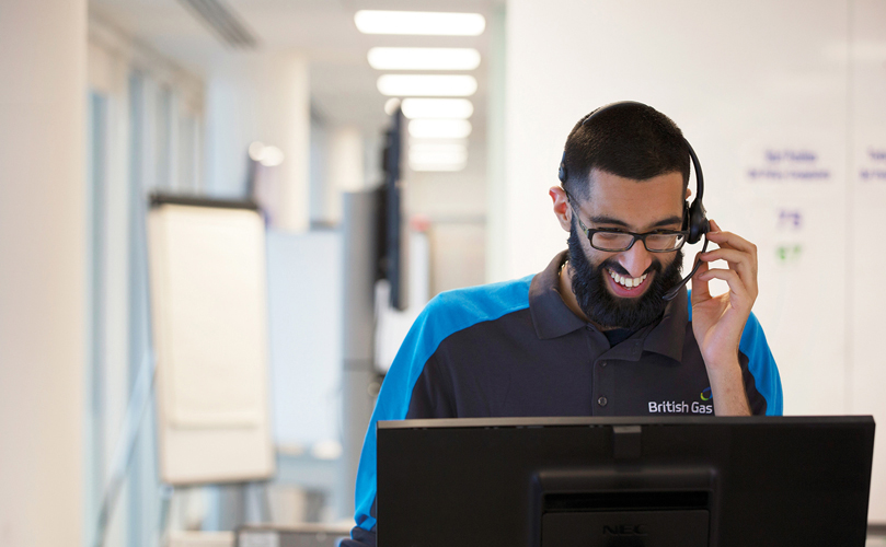 A worker smiling at his computer while talking with his headset