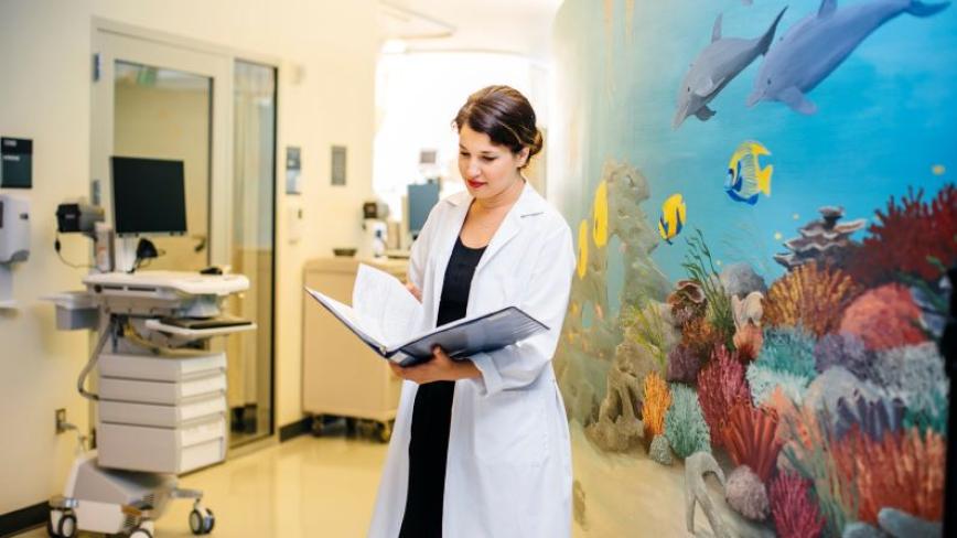 A person in a white coat standing inside a health care facility with a fish mural in the background