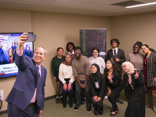 Dean Long holds his phone up to take a selfie with award winners and event coordinators inside a tan room