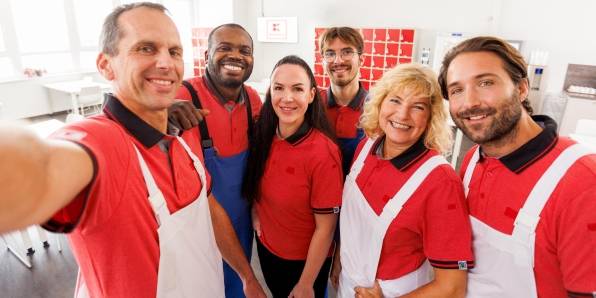 Ein Kaufland-Fleischwerk-Mitarbeiter macht mit seinen Kollegen ein Gruppenselfie im Pausenraum eines Kaufland-Fleischwerks.