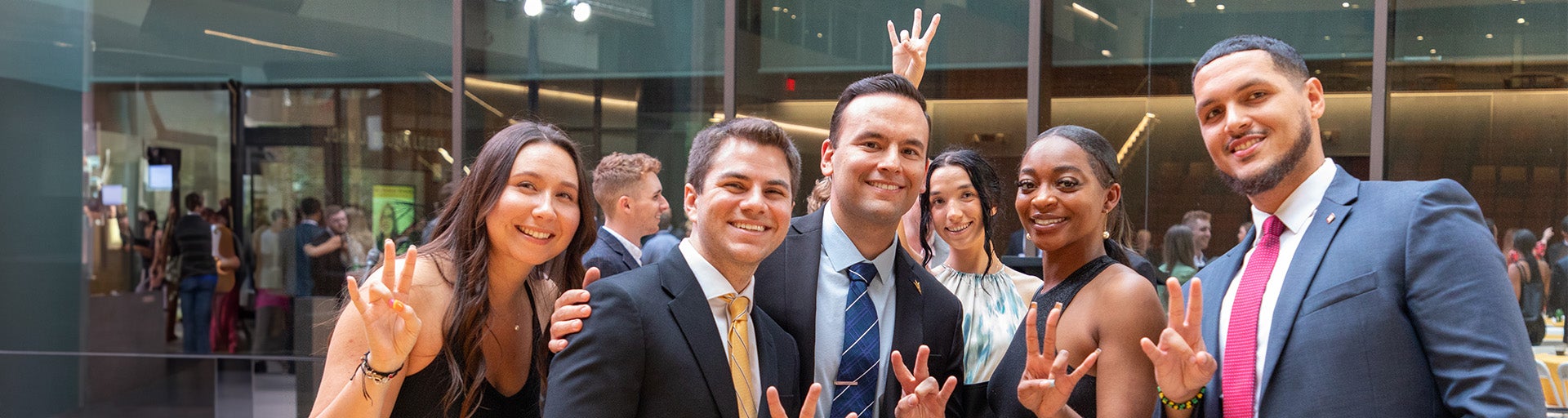 ASU Law recent graduates smiling and holding up the ASU pitchfork with their fingers.