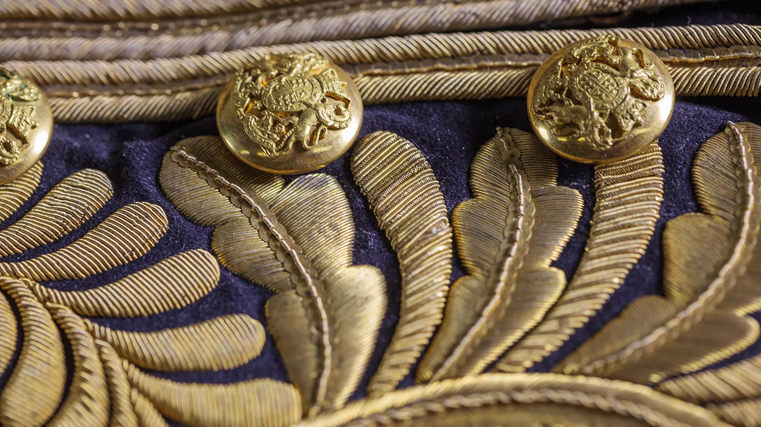 A close-up of an ornate coat with gold embroidered leaves and gold buttons embossed with the Australian coat of arms.