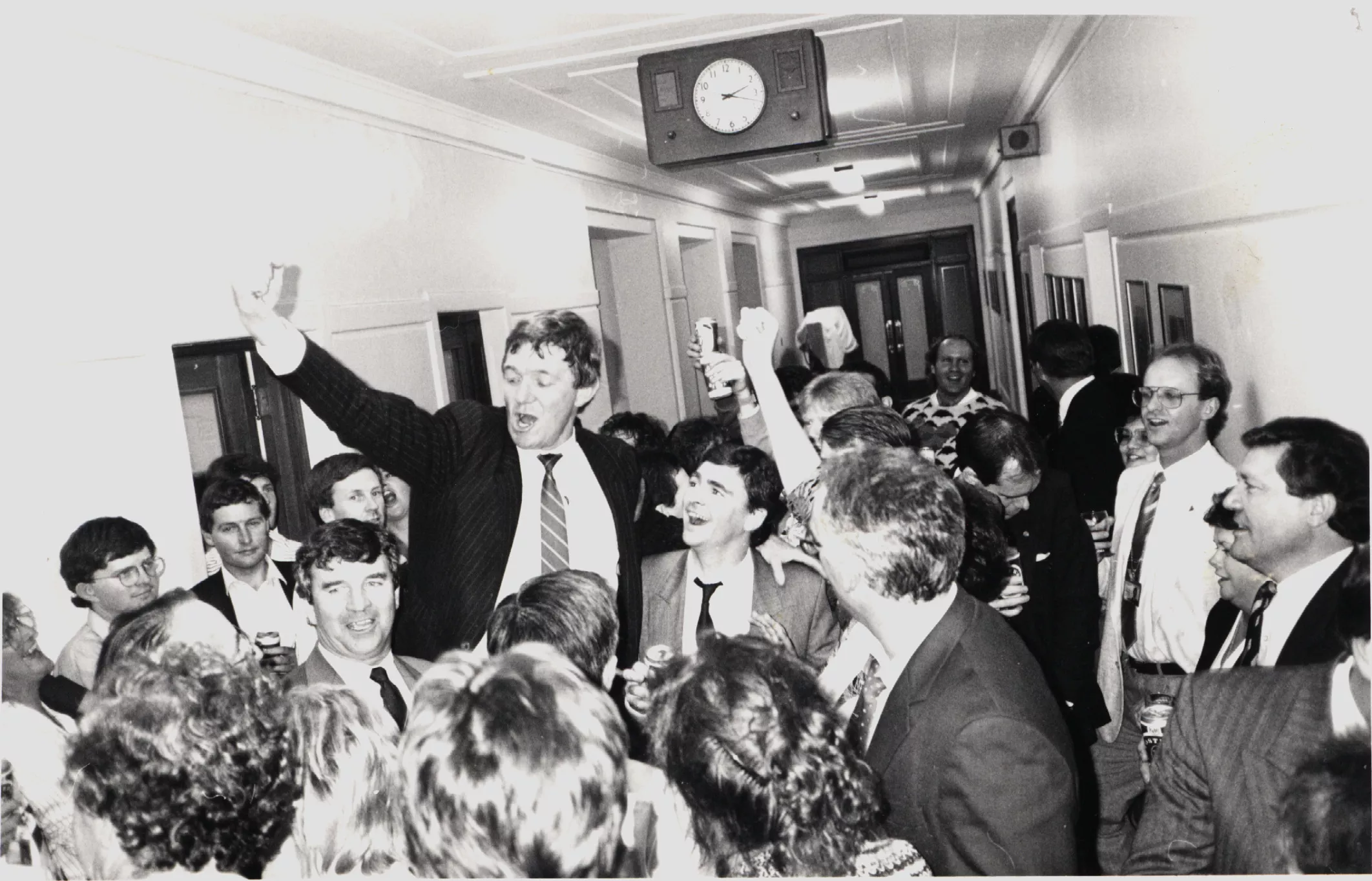 A black and white image of a corridor filled with people crowding around one person