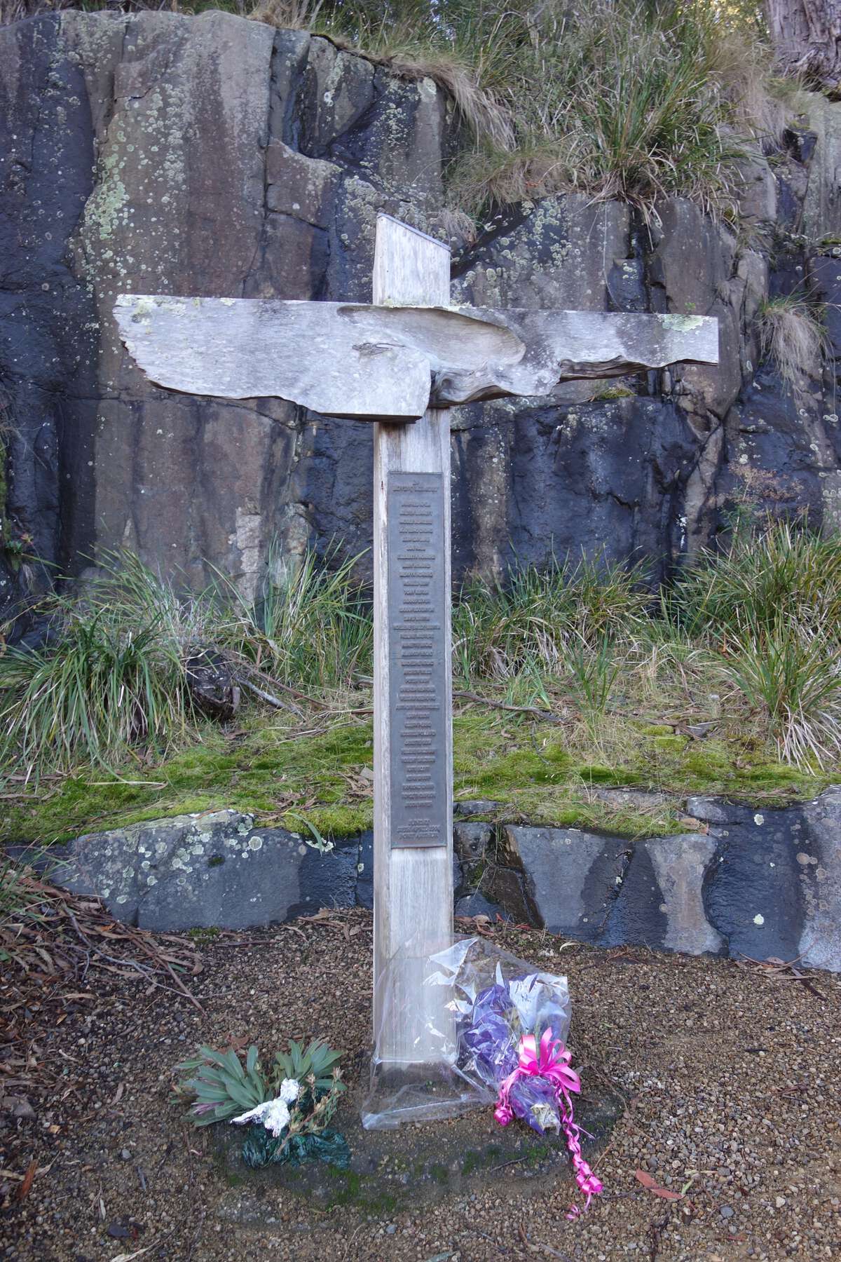 View of the Port Arthur Historic Site memorial garden in 2016. The garden was established at the site of the former Broad Arrow Café in 2000. This Huon pine memorial cross lists the names of the victims. It once stood at the water’s edge at the center of the historic site but was moved to the memorial garden in 2001 (see Frew 2012Frew, Elspeth A. 2012. “Interpretation of a Sensitive Heritage Site: The Port Arthur Memorial Garden, Tasmania.” International Journal of Heritage Studies 18 (1): 33–48.).  Image: Kristal Buckley 