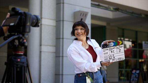 A student poses in front of a film camera with a clap board