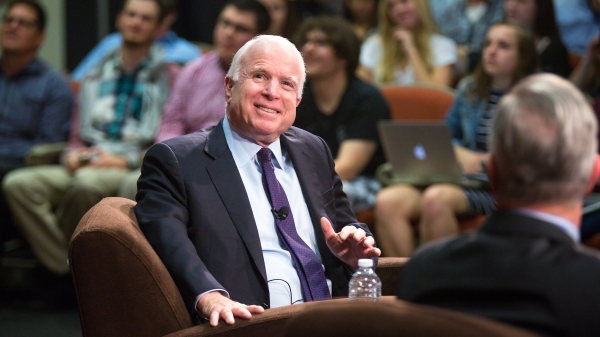 John McCain smiles while sitting in front of a crowd