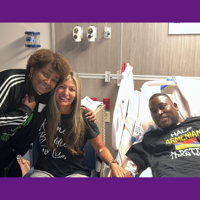 Todd smiles as he lays next in a hospital bed as his wife embraces Todd's living donor nearby.