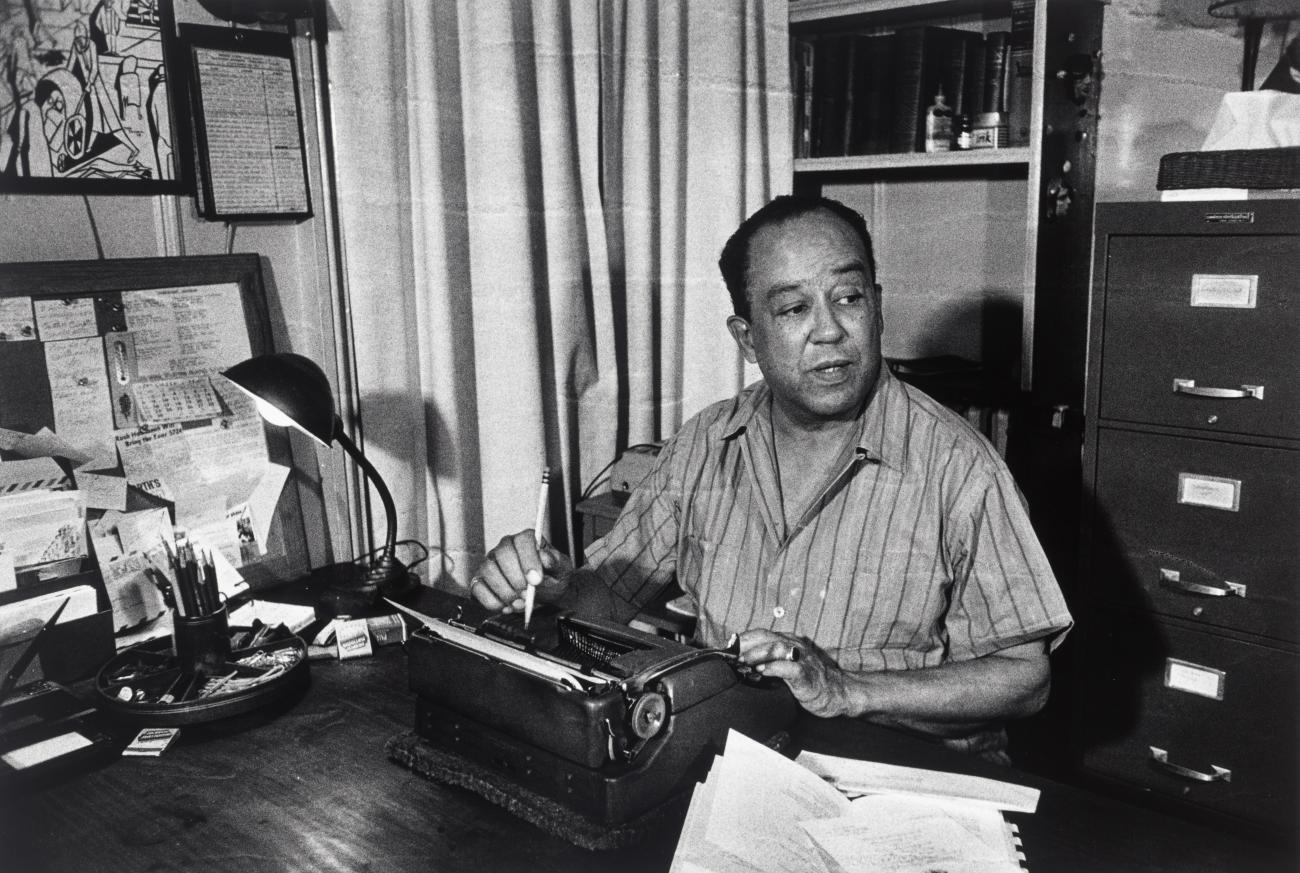 A portrait of Langston Hughes behind a desk