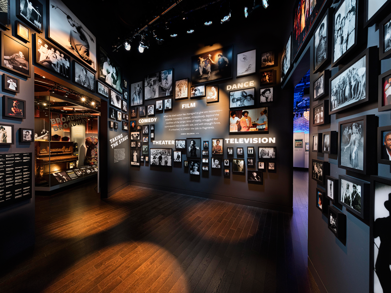 Entrance to Taking the Stage exhibition. Framed photographs of African American artists on the stage and screen are featured on the walls. 