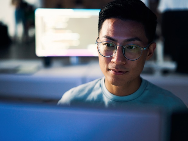 A programmer using a computer to write code in an office setting at nighttime.