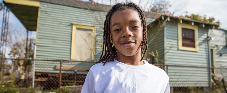 A boy smiles outside his house