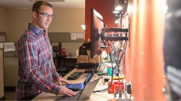 A person operating two computers at a raised desk