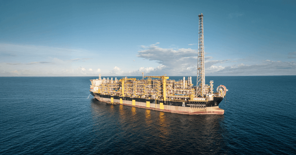 A floating production storage and offloading (FPSO) vessel on calm, open waters, showcasing its extensive industrial infrastructure under a clear sky.