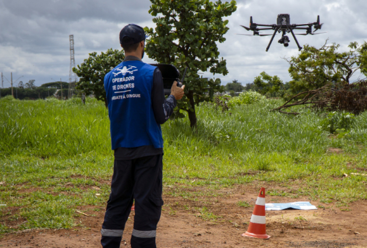 Operador de drones realiza mapeamento para combate à dengue em área verde.