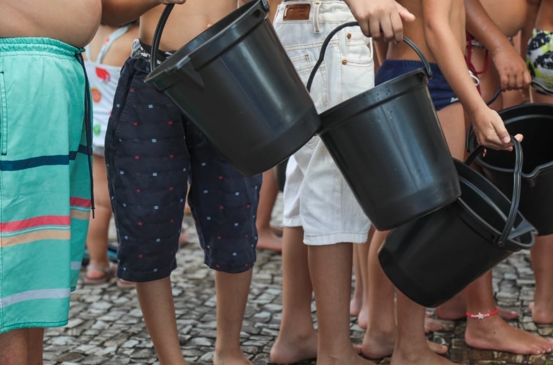 crianças seguram baldes pretos. 