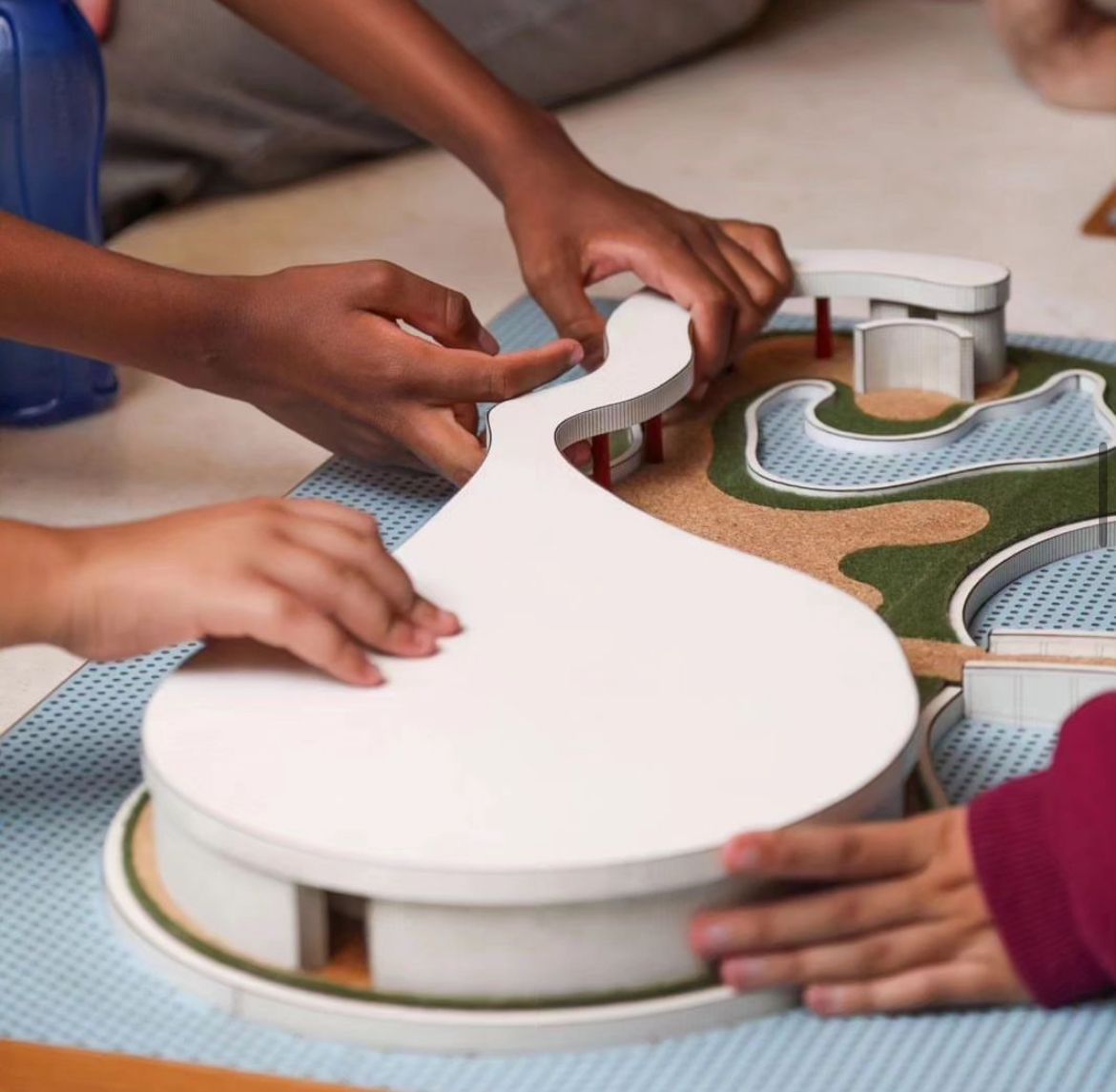 mãos de crianças tocam uma maquete da estrutura da Casa do Baile