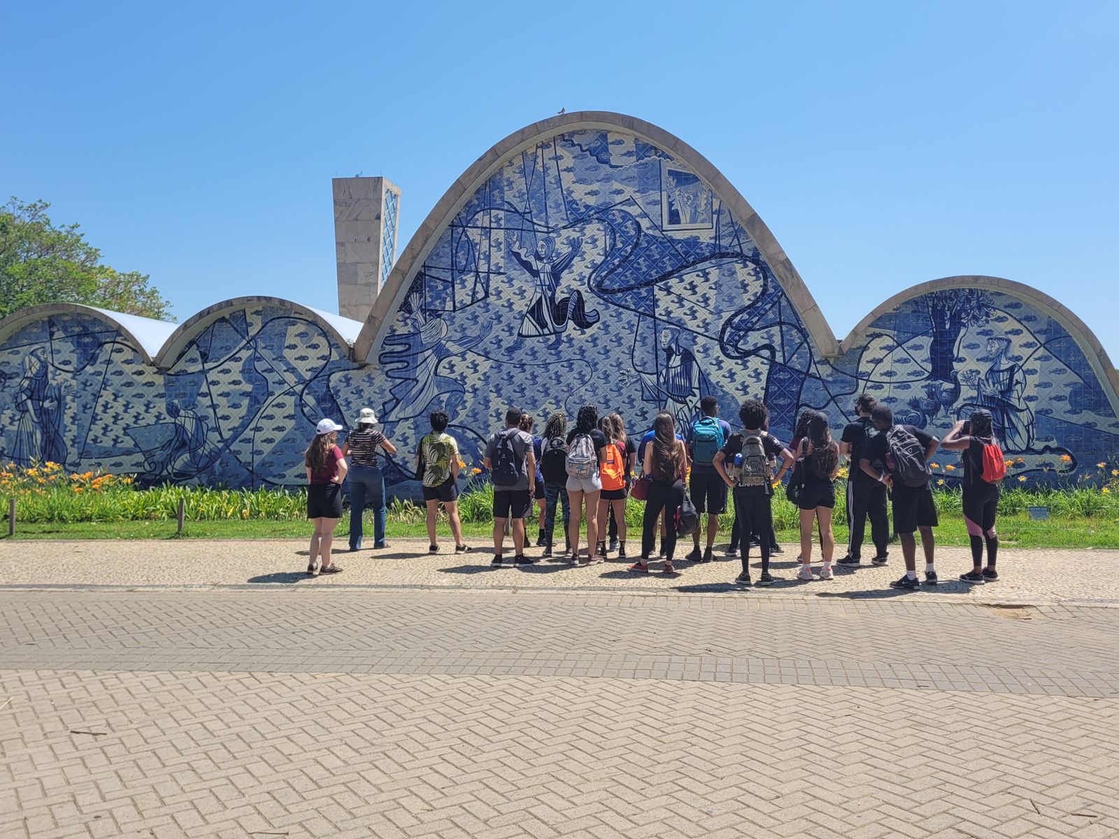 Aproximadamente 20 pessoas admiram a Igreja São Francisco de Assis. Elas estão de costas para câmera. 