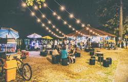 Cerca de vinte pessoas confraternizam ao lado do Centro de Referência Turística Álvaro Hardy - Veveco, durante a noite, na orla da Lagoa da Pampulha. Pessoas sentadas em mesas conversam, outras estão de pé, outras passeiam. Foto: Ricardo Laf