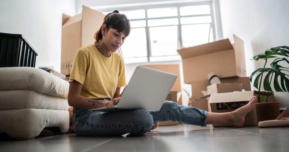 Woman sitting on floor amid moving boxes with a laptop