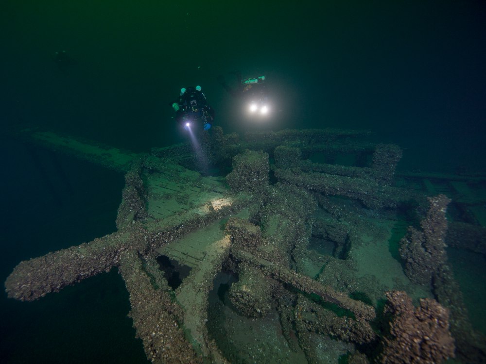 two scuba divers with bright lights swim over a shipwreck