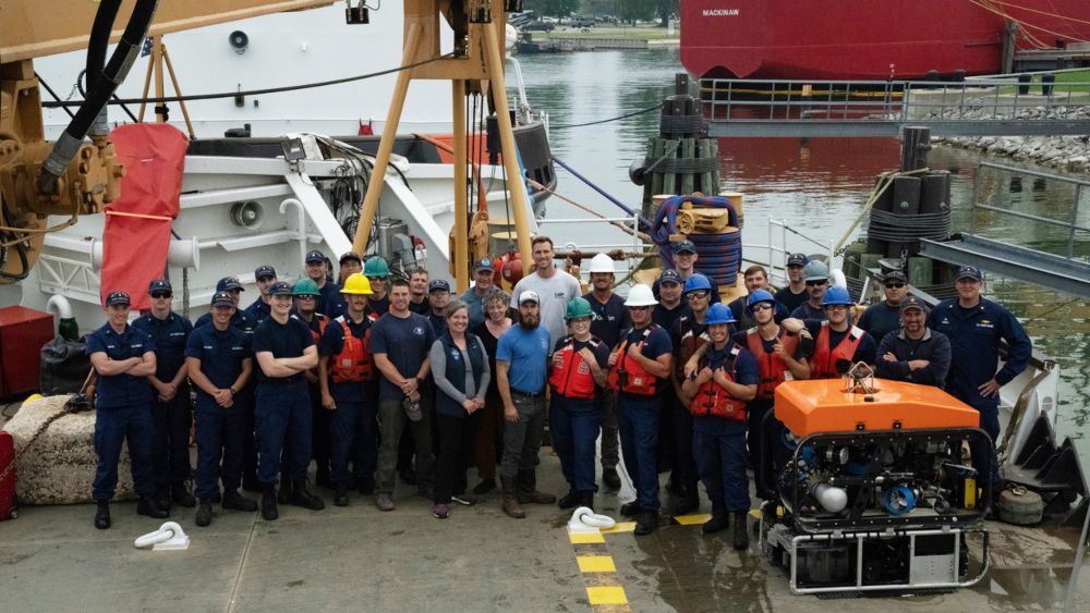 a group of people wearing hard hats stand together on a dock in front of a large ship