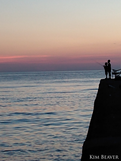 a silhouette of two children fishing from a steep cliff