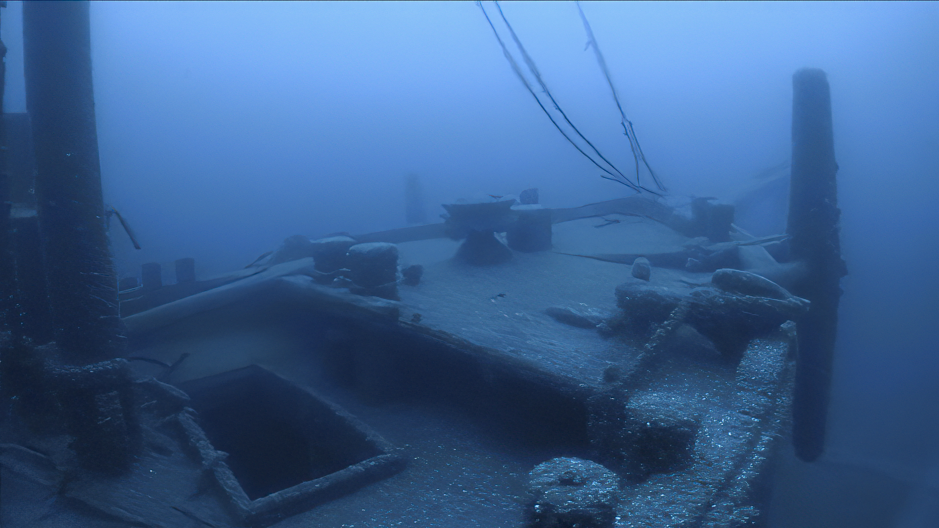 the deck of a wooden schooner vessel where the anchor is still visible near the bow. The forward mast is visible