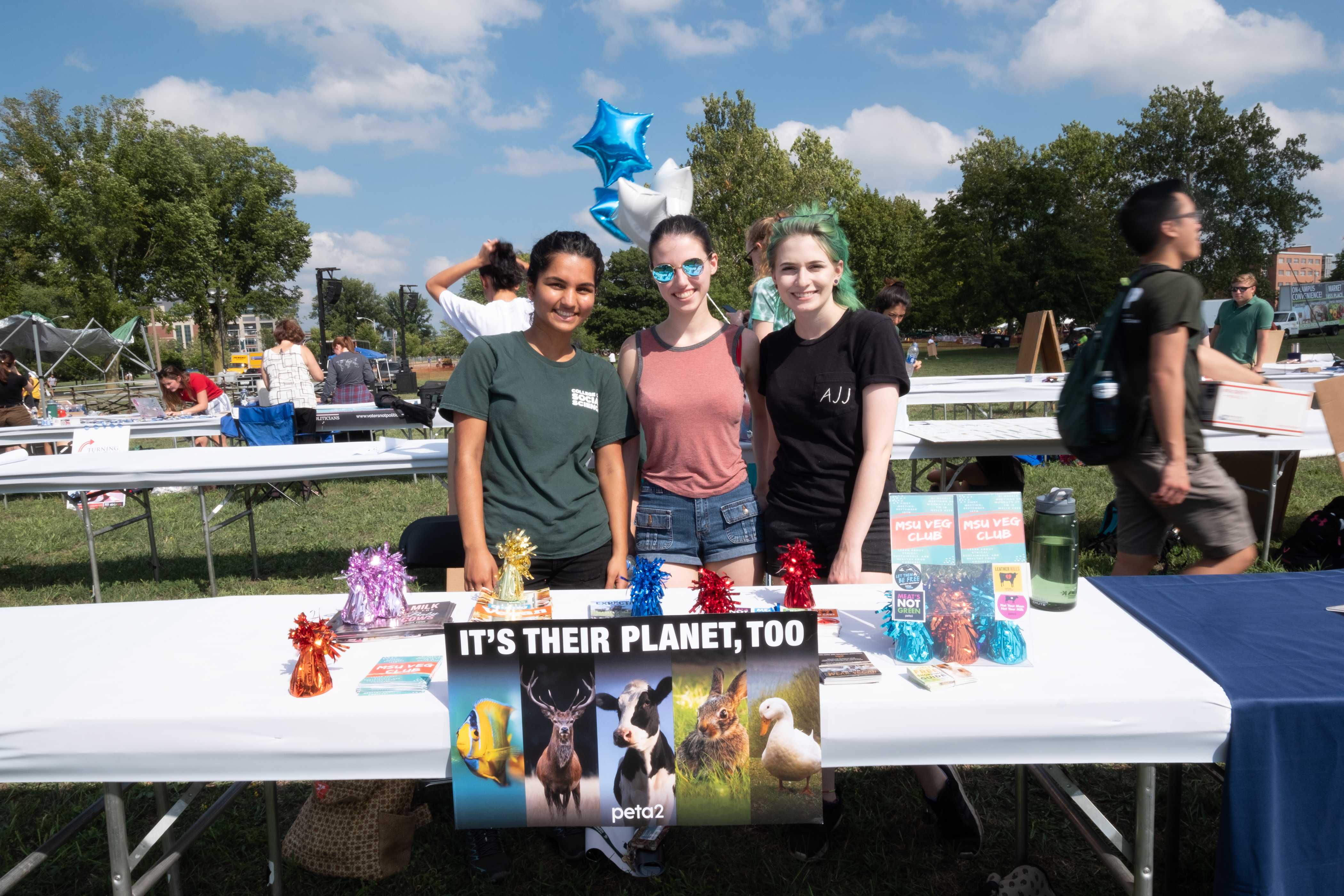 A small group of students looking at the camera smiling behind a table covered in promotional materials.