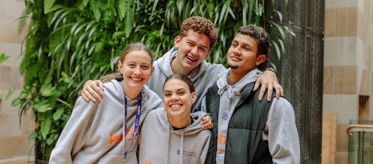 4 students smiling with plants behind them. 