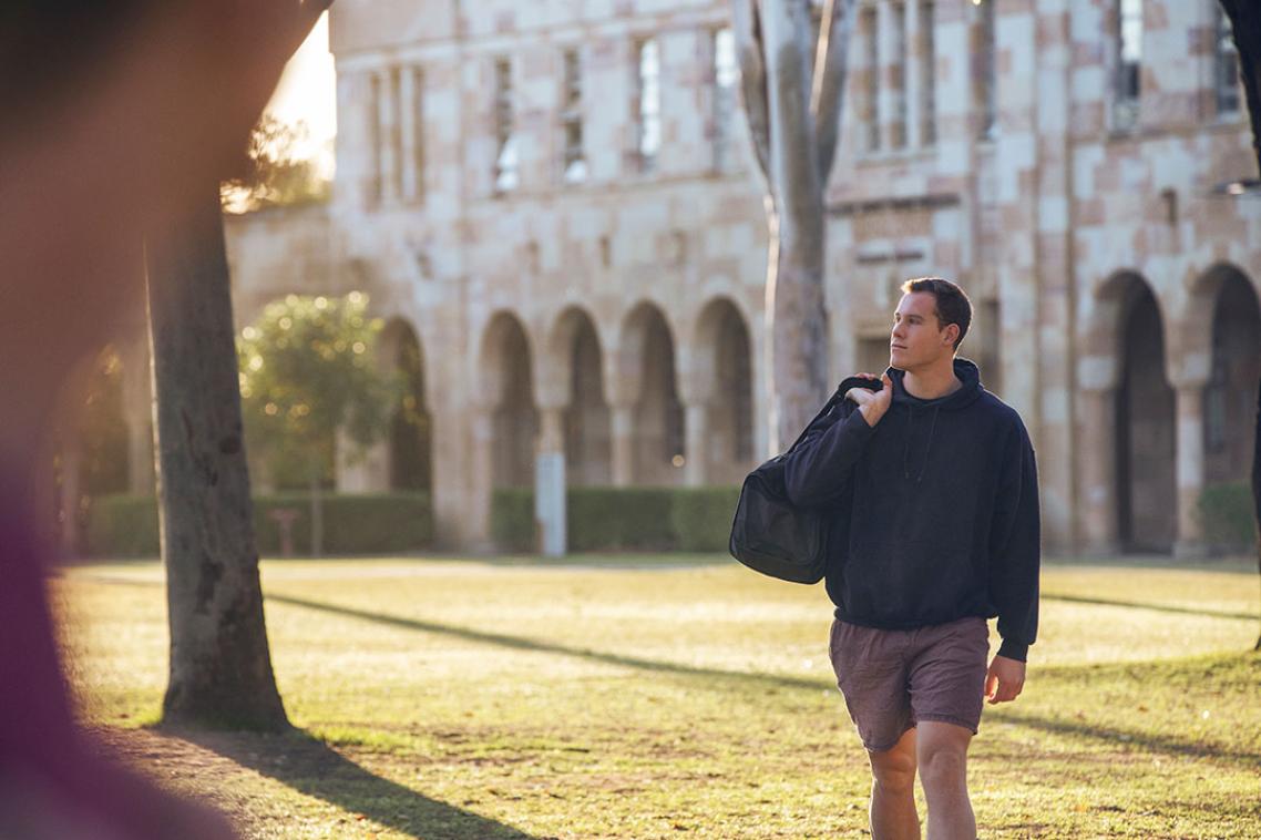 A student wearing a hoodie and shorts walking through the Great Court at sunrise.