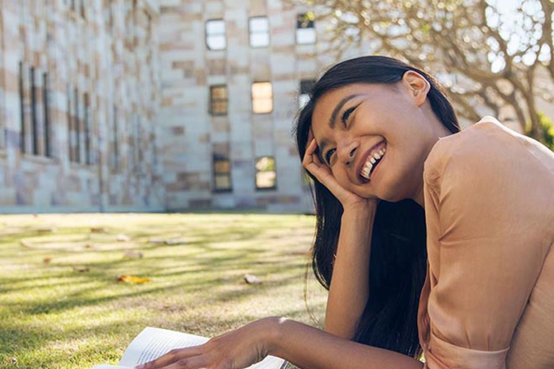 A student reading on the grass outside the Forgan Smith building at St Lucia campus.