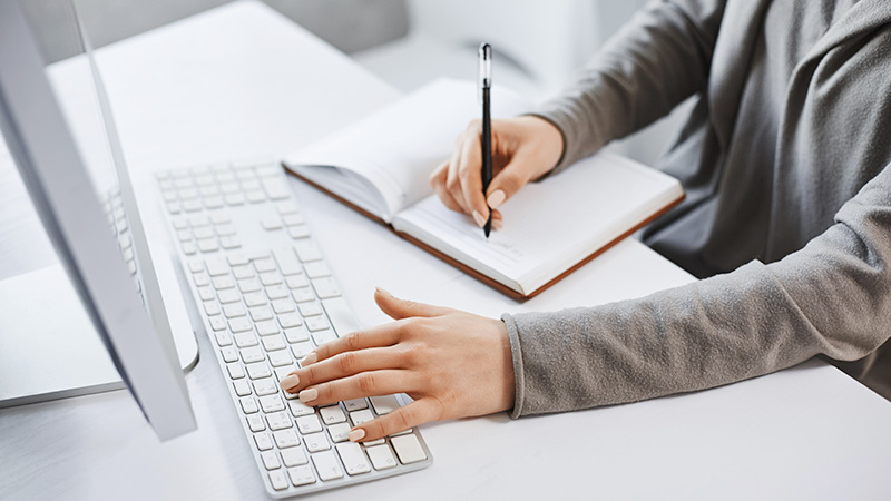 Person looking at computer screen and writing in notebook