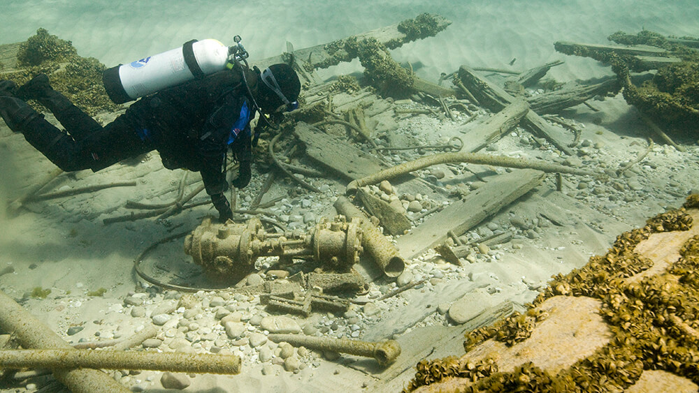 a diver swims above metal scraps and wood planks