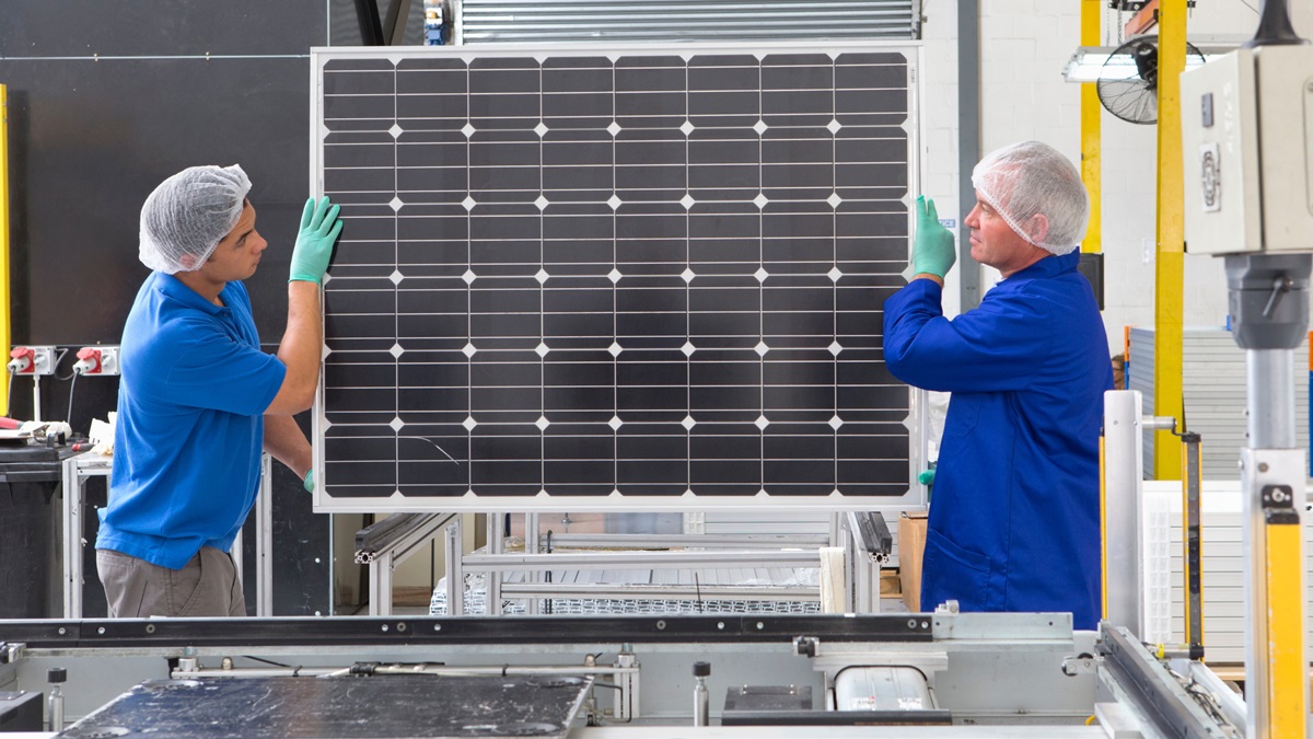 Factory workers lifting new solar panel from production line