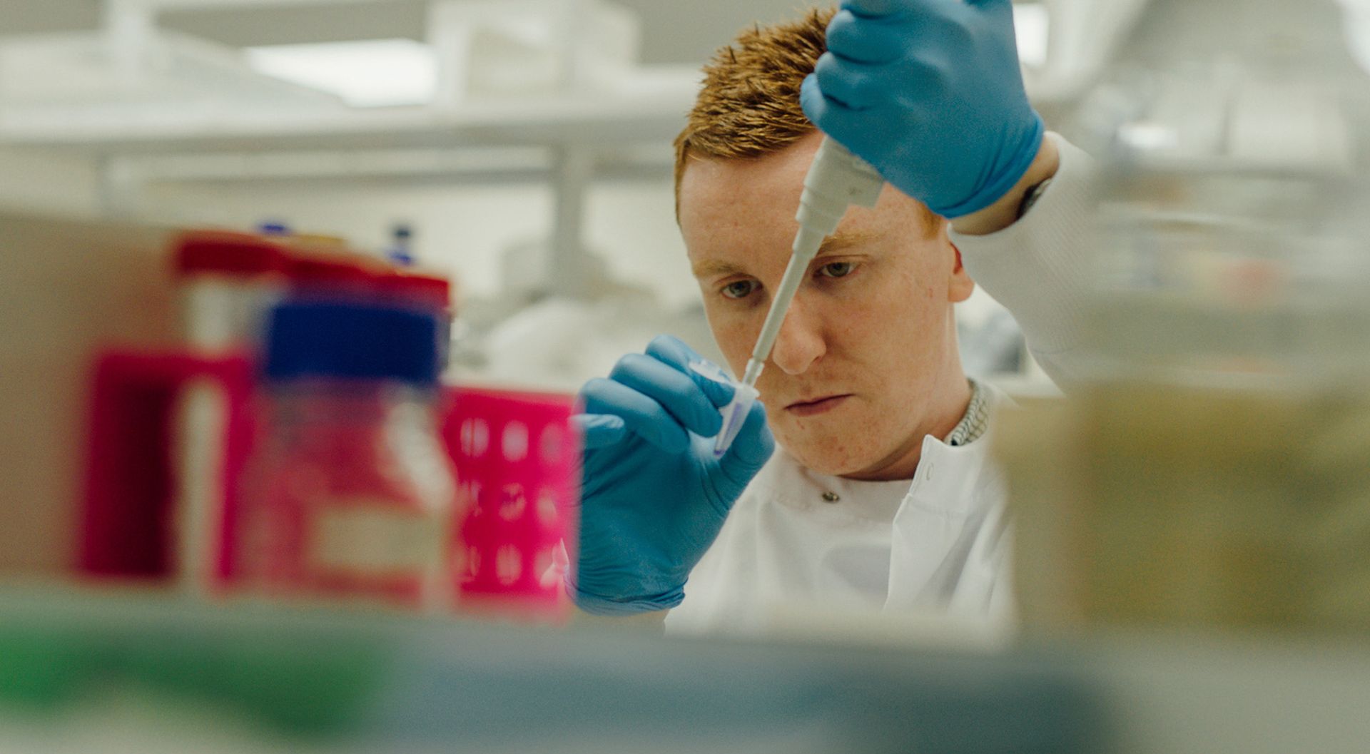 Scientist in a lab, looking intently at a laboratory dropper.