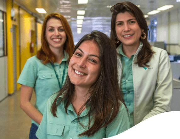 três mulheres posam para foto com uniforme verde da Vale, sorrindo