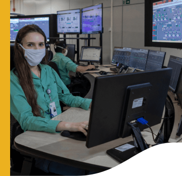 Vale employee wearing a protective mask, uniform, and badge. She is sitting in a room full of computers.