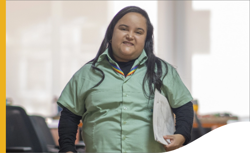 A woman is holding a briefcase under her arm and smiling for a photo. She is wearing a Vale uniform.