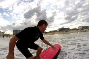 Guy wearing ear plugs surfs into the shallow water