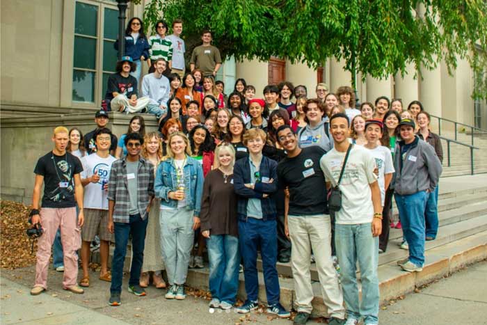 About 50 people pose for a group photo outside an MIT building