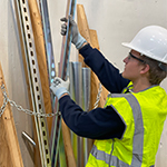 Hunter in a hard hat, safety vest and gloves selecting a piece of metal from a pile.